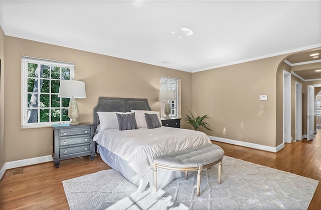 bedroom featuring baseboards, arched walkways, wood finished floors, and ornamental molding