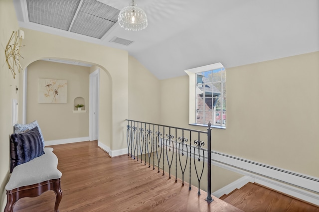 hallway with arched walkways, visible vents, vaulted ceiling, wood finished floors, and baseboards