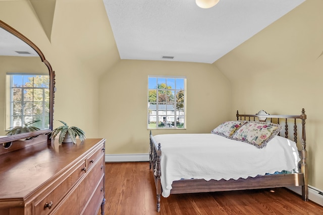 bedroom with a baseboard heating unit, lofted ceiling, dark wood-style flooring, and visible vents