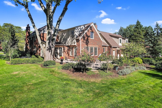 rear view of property with a yard, a patio area, brick siding, and a chimney