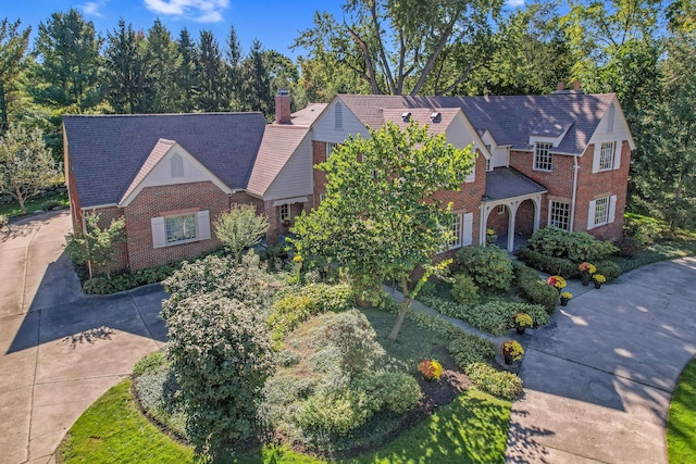 view of front of house featuring driveway, brick siding, and a chimney