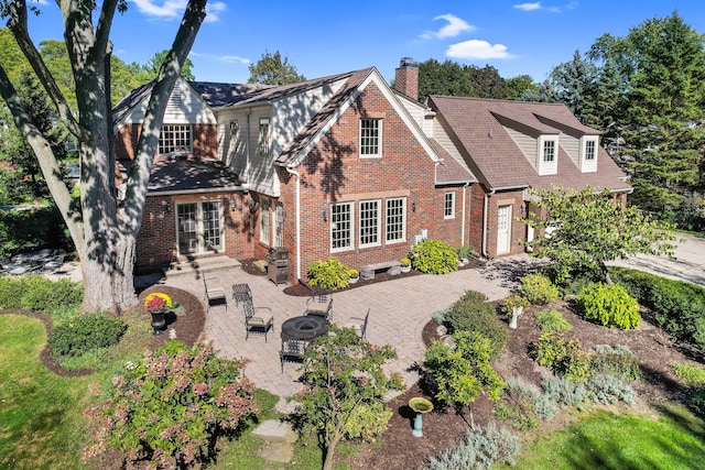 view of front of home featuring entry steps, brick siding, decorative driveway, a chimney, and a patio area