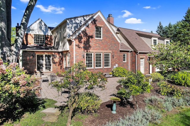 rear view of property featuring a chimney, roof with shingles, french doors, a patio area, and brick siding