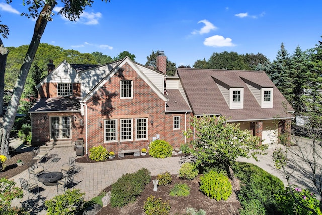 view of front facade with a garage, brick siding, a patio, and a chimney