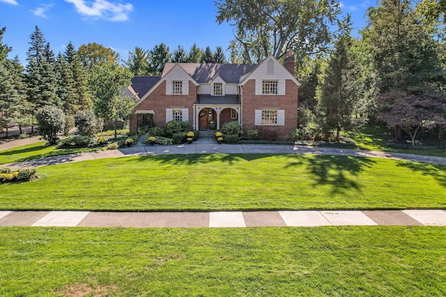 view of front of property with a front yard, a chimney, and brick siding