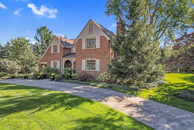 view of front of property with driveway, a front yard, a chimney, and brick siding