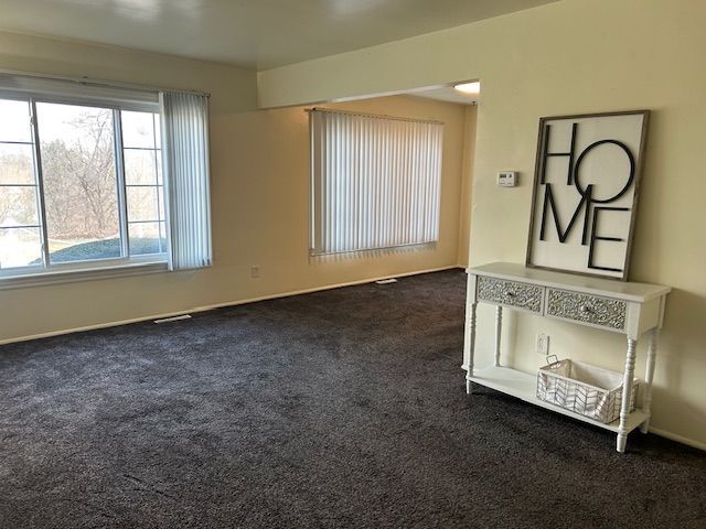 empty room featuring dark colored carpet, visible vents, and baseboards