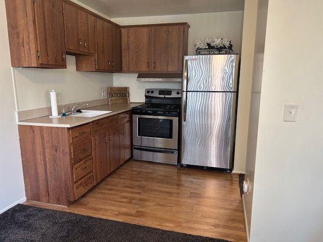 kitchen featuring light wood-style flooring, under cabinet range hood, stainless steel appliances, a sink, and light countertops