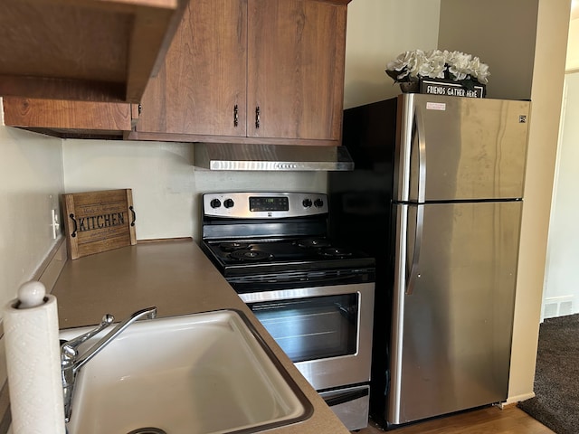 kitchen featuring stainless steel appliances, visible vents, brown cabinetry, a sink, and wall chimney exhaust hood