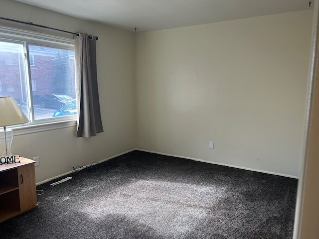 spare room featuring dark colored carpet and baseboards