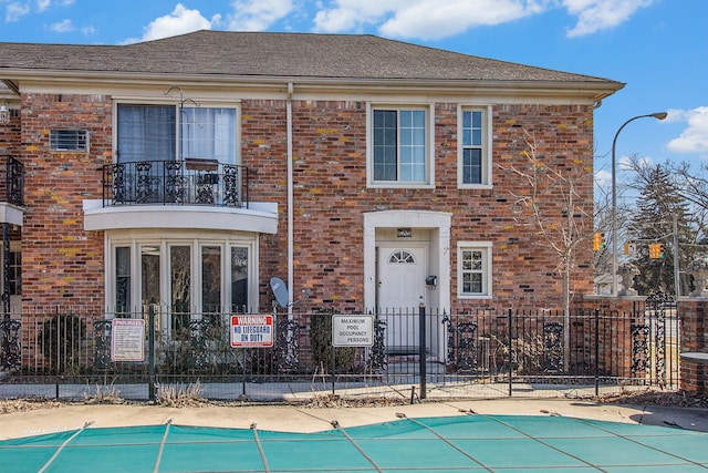 view of front of property with brick siding, fence, a balcony, and a community pool