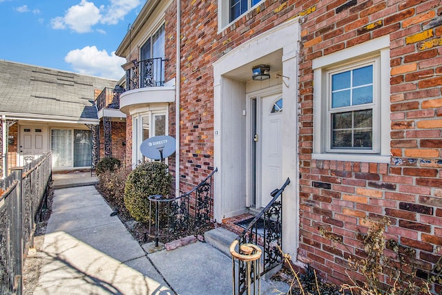 entrance to property featuring a balcony, fence, and brick siding