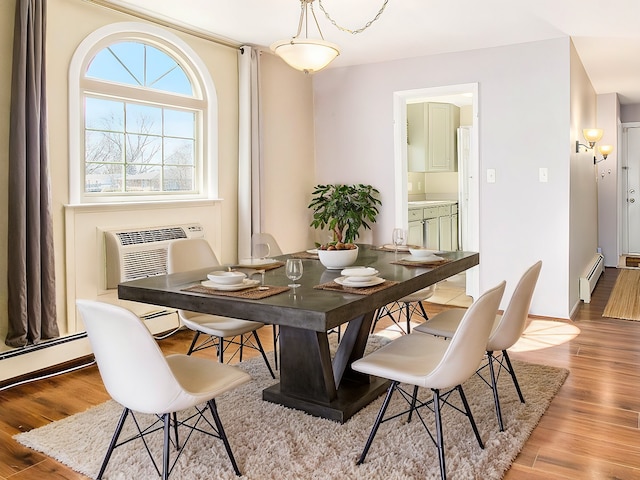 dining space with a baseboard heating unit, an AC wall unit, and wood finished floors