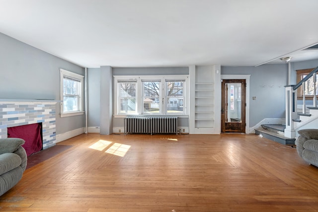 living room featuring radiator heating unit, a fireplace, stairway, and baseboards