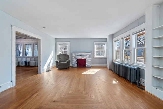 unfurnished room with baseboards, a fireplace with flush hearth, visible vents, and radiator