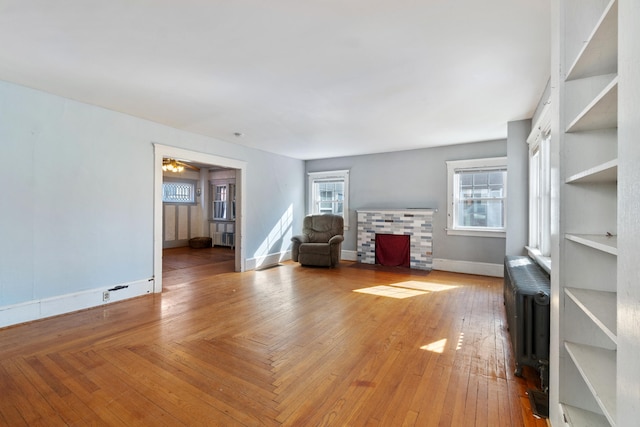 unfurnished living room featuring radiator, plenty of natural light, a fireplace with flush hearth, and hardwood / wood-style floors