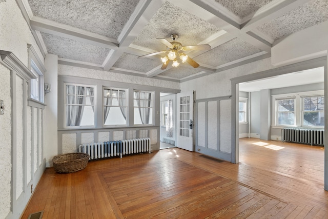 unfurnished room featuring beam ceiling, wood-type flooring, coffered ceiling, and radiator heating unit