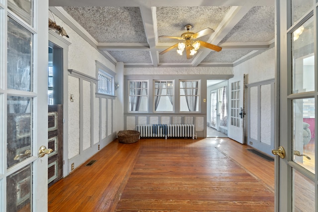 unfurnished sunroom featuring radiator, visible vents, ceiling fan, coffered ceiling, and beamed ceiling