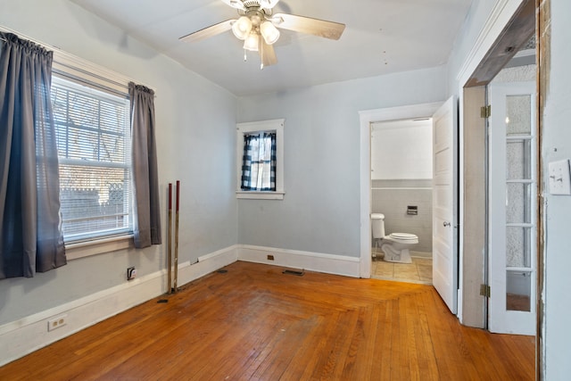 unfurnished bedroom featuring hardwood / wood-style flooring, multiple windows, baseboards, and a ceiling fan