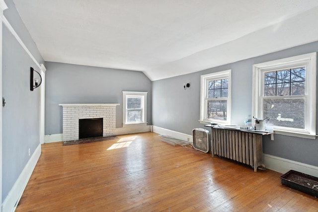 living room with a fireplace, radiator, hardwood / wood-style floors, vaulted ceiling, and baseboards