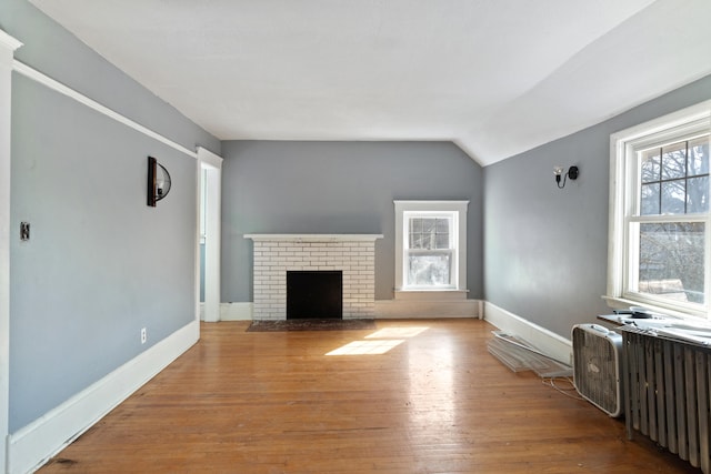 unfurnished living room with lofted ceiling, radiator, a brick fireplace, wood finished floors, and baseboards