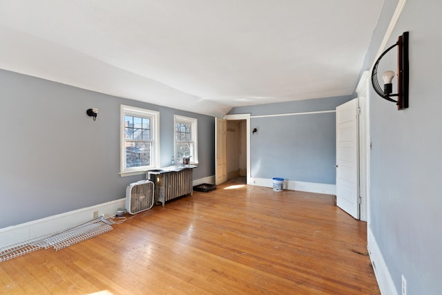 empty room with vaulted ceiling, radiator heating unit, light wood-type flooring, and baseboards