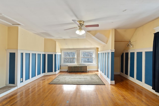 additional living space with vaulted ceiling, radiator heating unit, wood-type flooring, and a ceiling fan