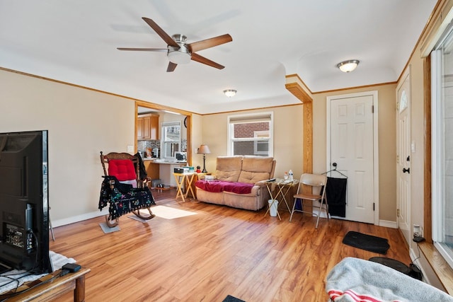 living area featuring ornamental molding, baseboards, ceiling fan, and light wood finished floors