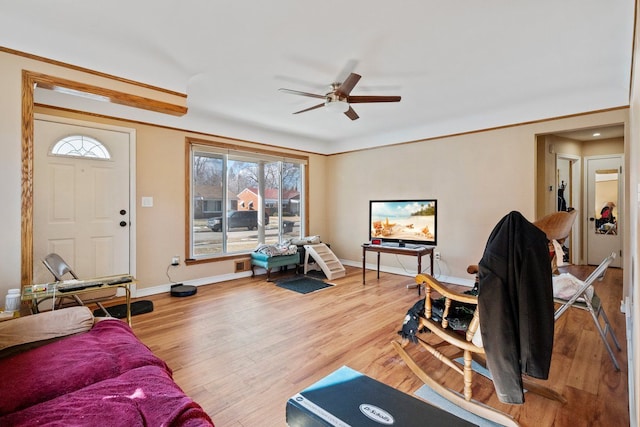 living area featuring a ceiling fan, crown molding, baseboards, and wood finished floors