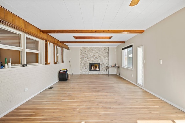 unfurnished living room featuring light wood-style floors, beam ceiling, a fireplace, and brick wall