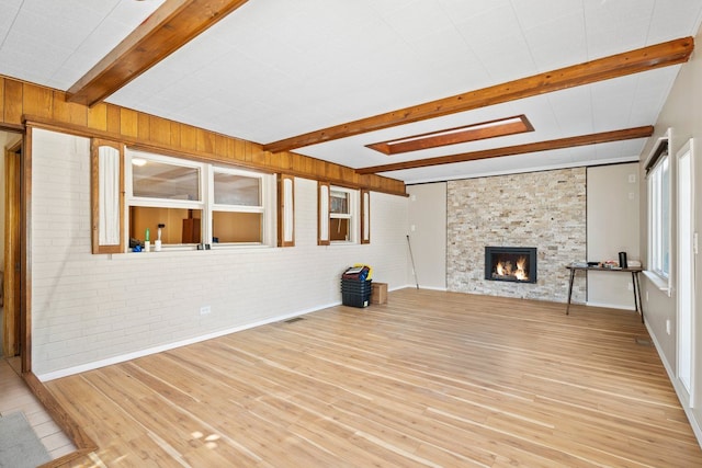 unfurnished living room with beam ceiling, a stone fireplace, brick wall, and wood finished floors