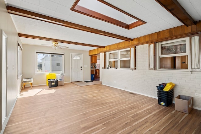 interior space featuring visible vents, light wood-style floors, a ceiling fan, brick wall, and beamed ceiling