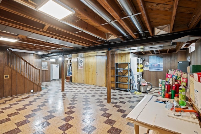 unfinished below grade area with stairway, freestanding refrigerator, wooden walls, and tile patterned floors