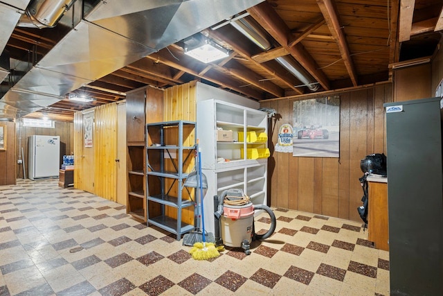 unfinished basement with freestanding refrigerator, wooden walls, and tile patterned floors