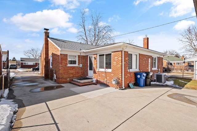 view of front of house featuring a chimney, central AC unit, and brick siding