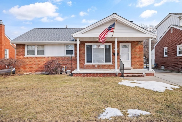 bungalow-style house with covered porch, a shingled roof, a front lawn, and brick siding