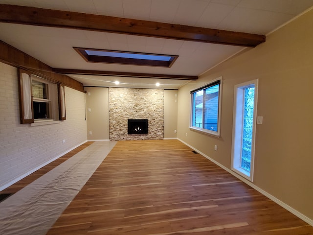 unfurnished living room with baseboards, brick wall, beamed ceiling, wood finished floors, and a fireplace