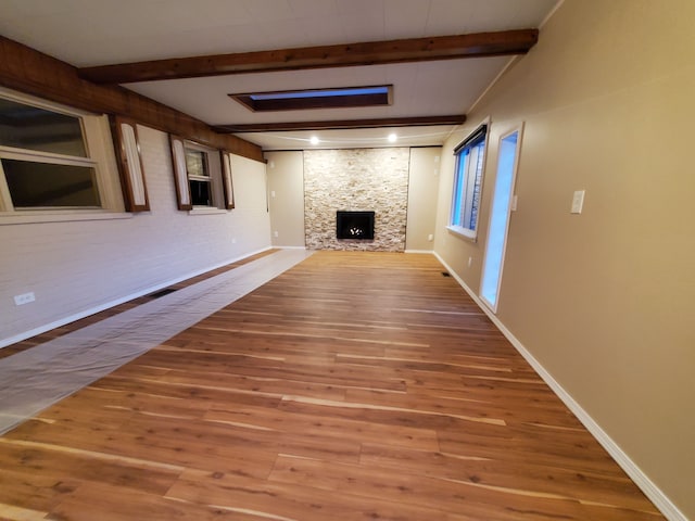 unfurnished living room featuring a fireplace, wood finished floors, beam ceiling, and baseboards