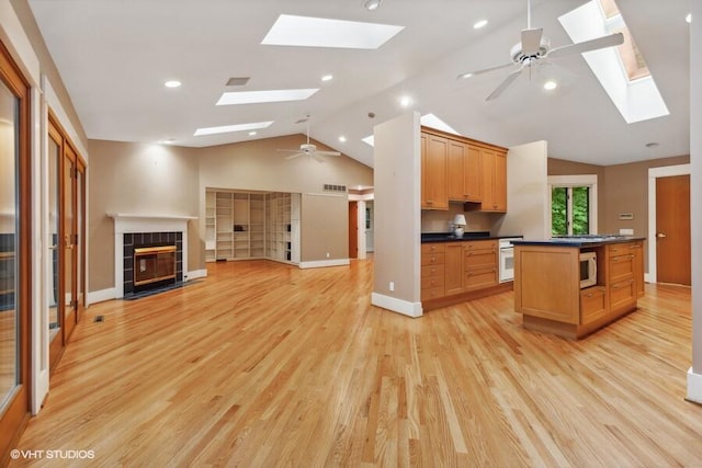 kitchen featuring white microwave, a tile fireplace, a ceiling fan, open floor plan, and dark countertops