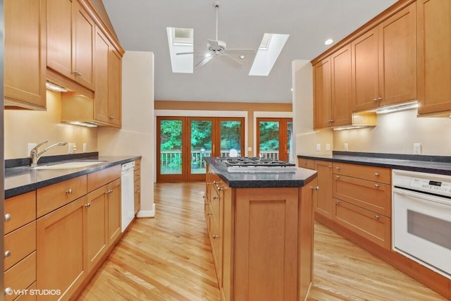 kitchen with white appliances, a ceiling fan, a kitchen island, light wood-type flooring, and a sink