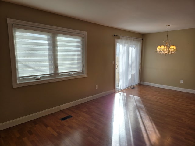 unfurnished room with visible vents, a notable chandelier, baseboards, and wood finished floors