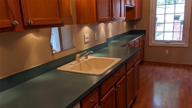 kitchen featuring dark countertops, baseboards, a sink, and wood finished floors