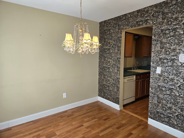 unfurnished dining area with dark wood finished floors, a notable chandelier, a sink, and baseboards