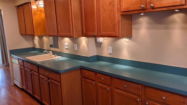 kitchen with dark wood-style floors, dark countertops, brown cabinetry, a sink, and dishwasher