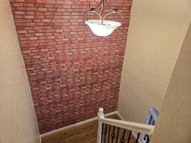 staircase with brick wall, wood finished floors, and baseboards