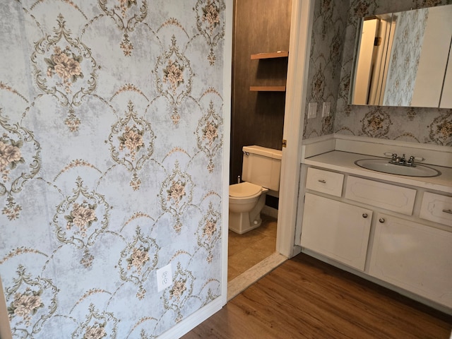 bathroom featuring wallpapered walls, vanity, toilet, and wood finished floors