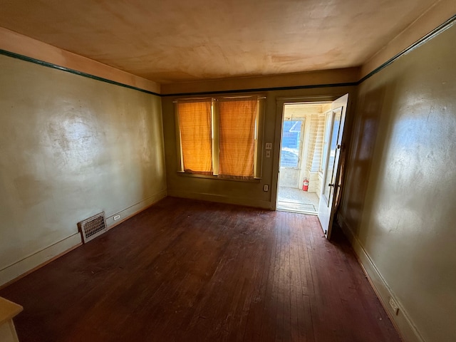 empty room featuring dark wood-type flooring, visible vents, and baseboards