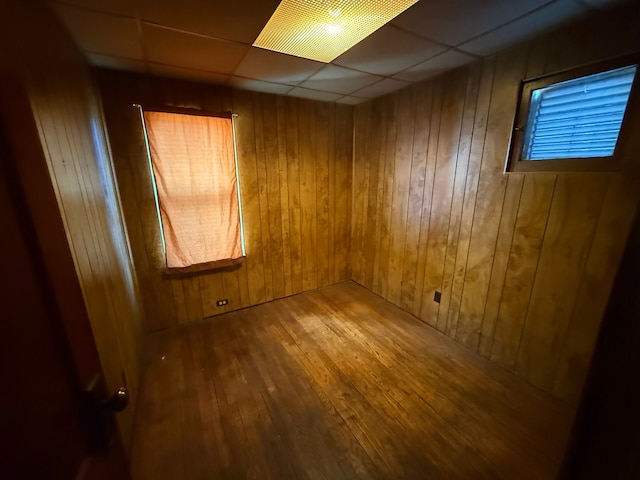 unfurnished room with a drop ceiling, wood walls, wood-type flooring, and elevator