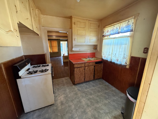 kitchen with white gas stove, wainscoting, a sink, and under cabinet range hood