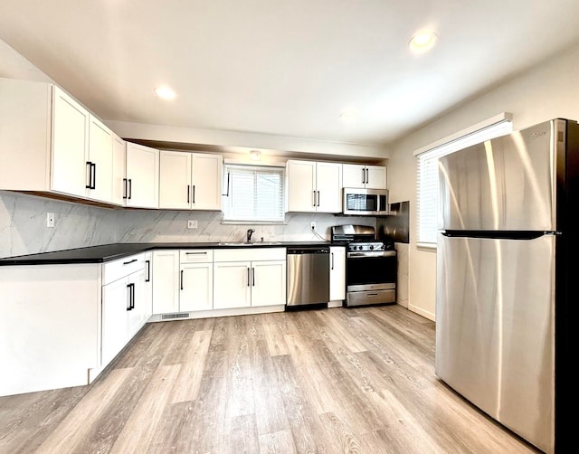 kitchen with a sink, white cabinetry, appliances with stainless steel finishes, light wood finished floors, and dark countertops